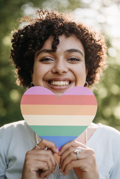 Free Woman smiling and holding a rainbow heart cutout, symbolizing LGBTQ+ pride. Stock Photo