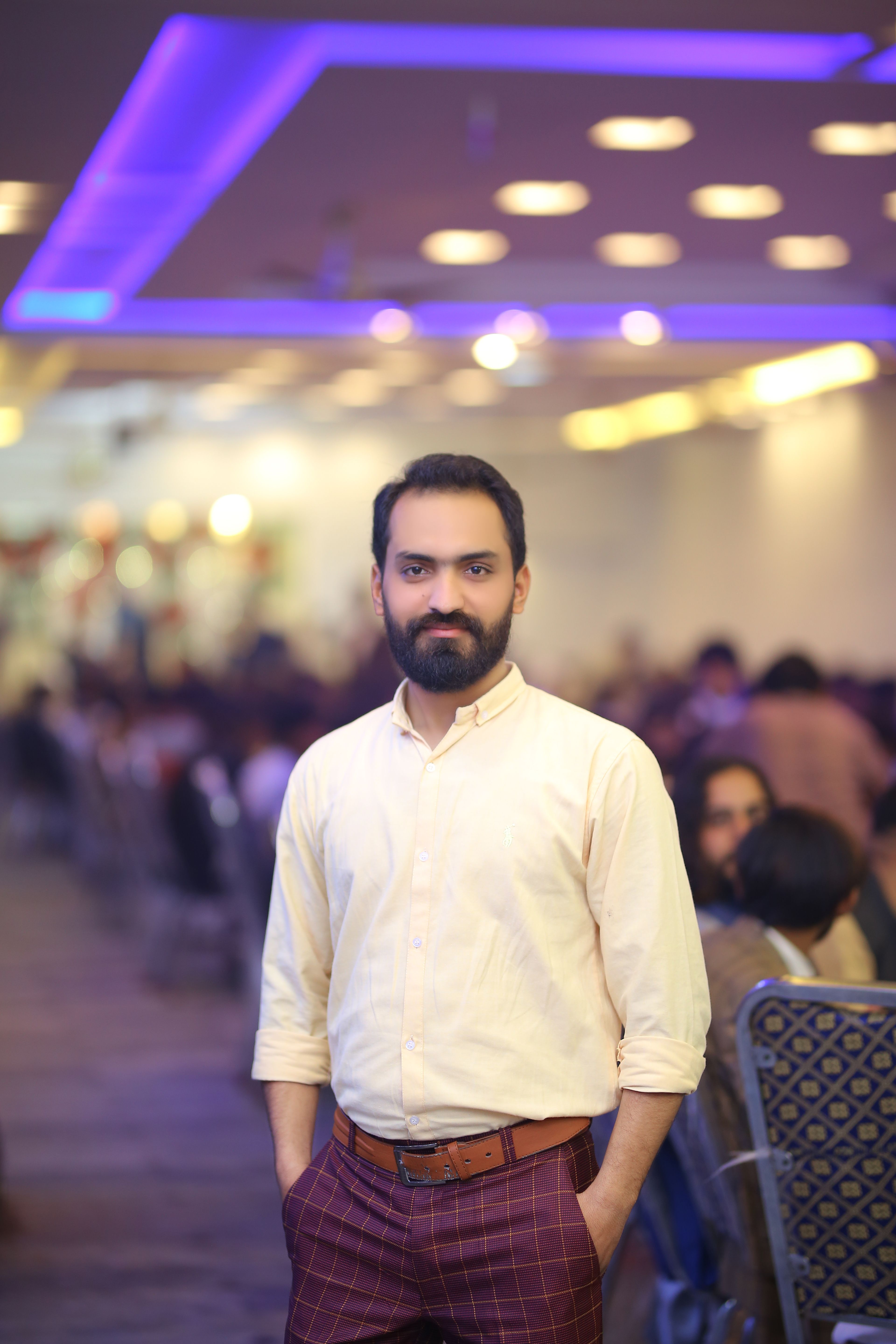 A confident man with a beard standing in a vibrant indoor conference venue.