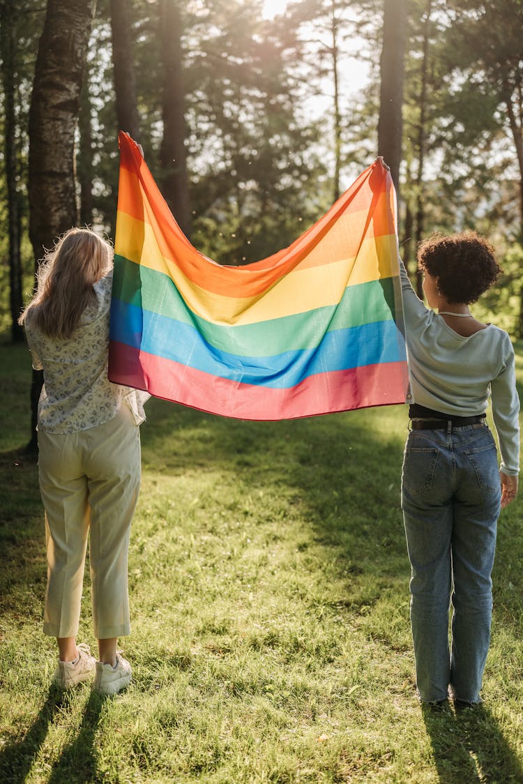 Back View Of Two Women In A Park Holding A Rainbow Flag