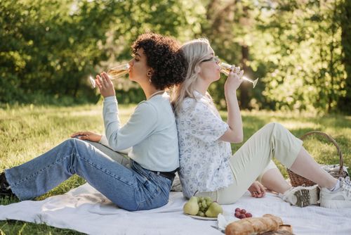 Free Couple enjoying a romantic outdoor picnic with wine and fruits on a sunny day. Stock Photo