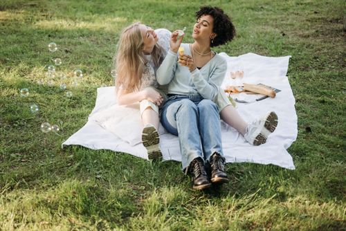 Free Two friends blow bubbles and enjoy a sunny picnic outdoors. Stock Photo