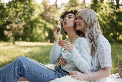 Free A joyful couple blowing bubbles outdoors, celebrating love and togetherness during a picnic. Stock Photo