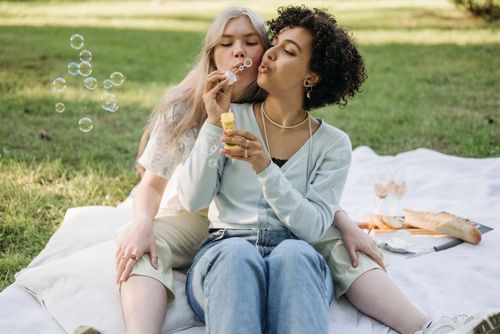 Free Two women enjoying a picnic on a sunny day, blowing bubbles and sharing affection outdoors. Stock Photo