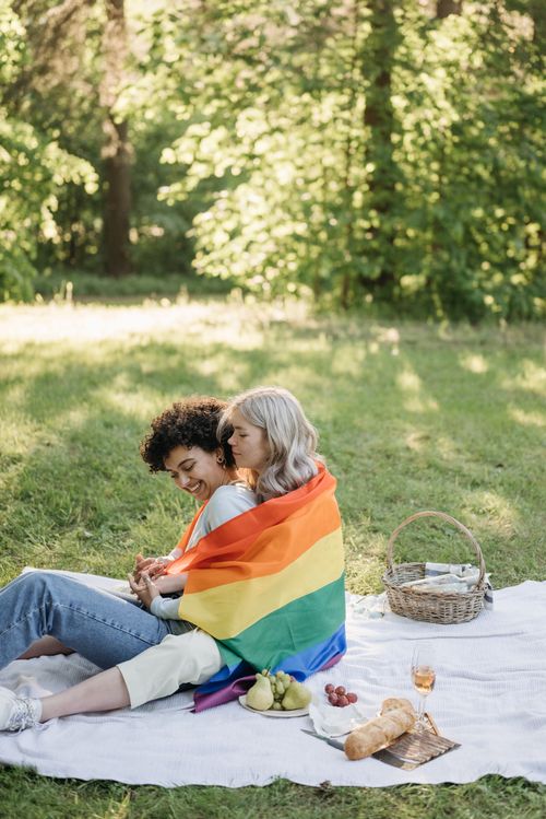 Free A happy couple enjoys a romantic picnic wrapped in a rainbow flag in a sunny park. Stock Photo