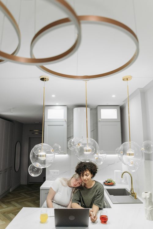 Free A couple enjoys a moment together in a stylish modern kitchen with pendant lighting and a laptop. Stock Photo