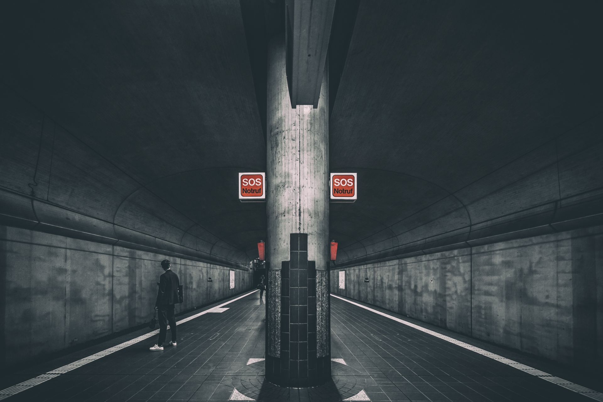 A solitary figure stands in a moody underground subway station, emphasized by prominent SOS signage.