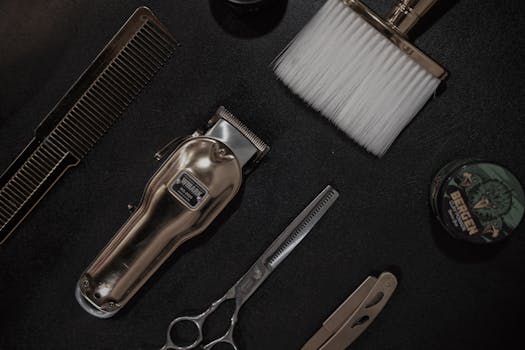 Flat lay of barber tools including clipper, scissors, and comb on a black surface.