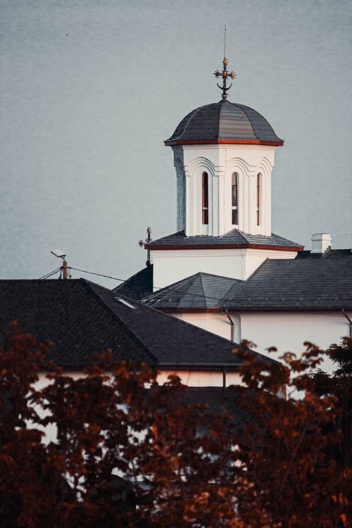 Free Vertical shot of a traditional church tower amidst autumn tree crowns, showcasing architectural elegance. Stock Photo