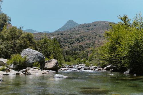 Free Peaceful river flowing through a lush mountain landscape under a clear blue sky. Stock Photo