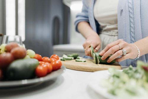 Free Close-up of a woman slicing cucumbers on a wooden board surrounded by fresh vegetables. Stock Photo