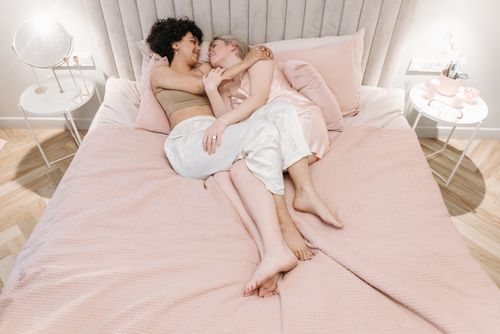 Free Two women lovingly embrace on a bed with pastel pink sheets, conveying intimacy and love. Stock Photo