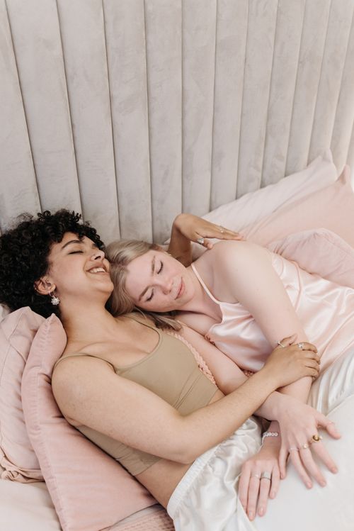Free A loving same-sex couple embracing and smiling in a cozy bedroom scene. Stock Photo
