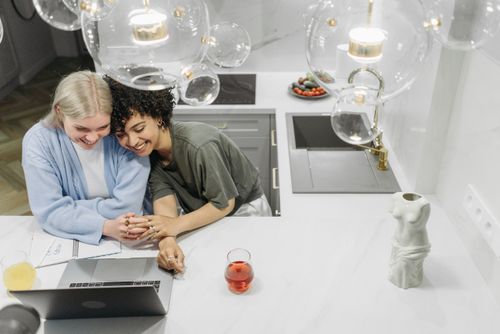 Free A joyful lesbian couple bonding and working on a laptop in a contemporary kitchen setting. Stock Photo