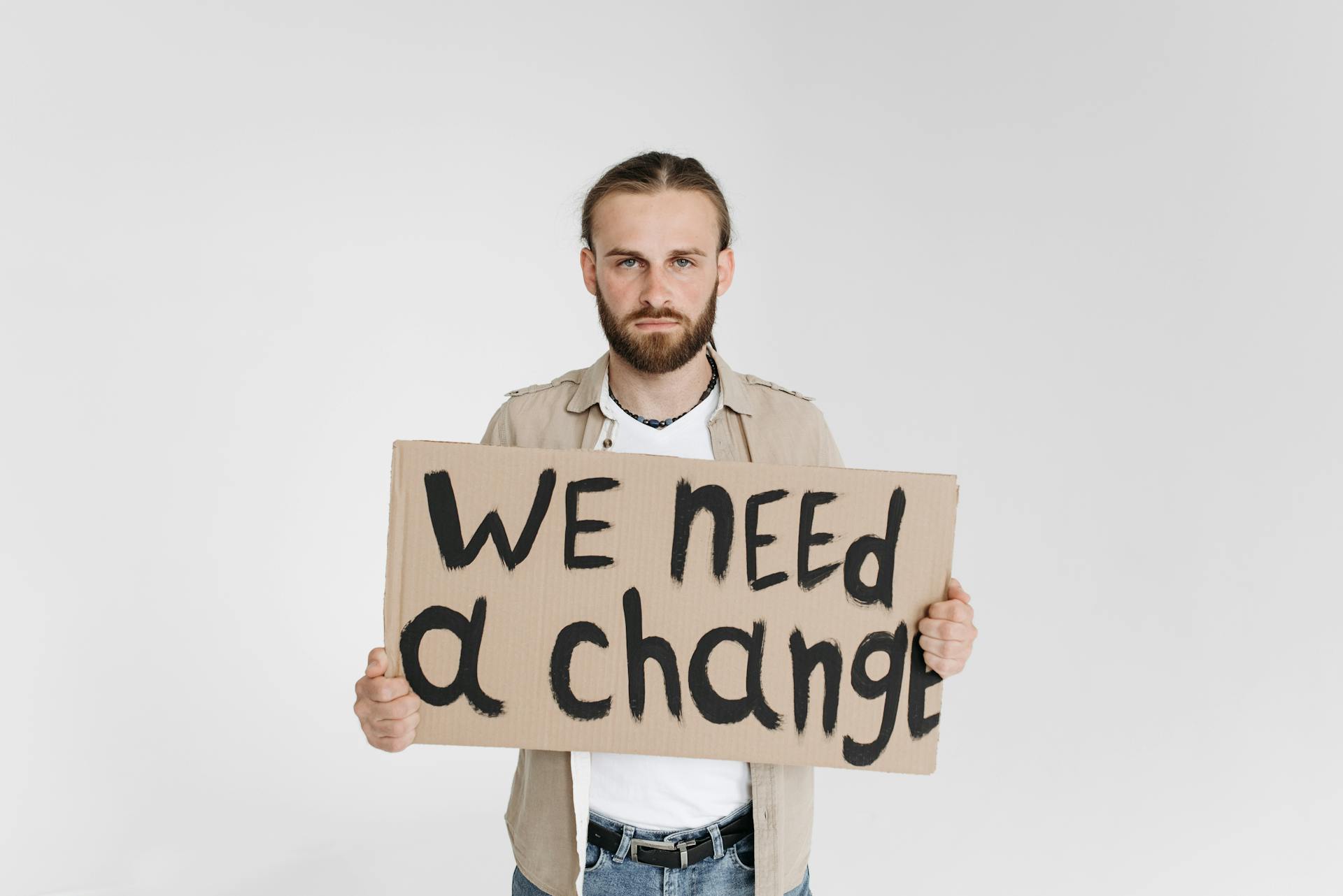 A man holding a protest sign reading 'We Need a Change' on a white background.