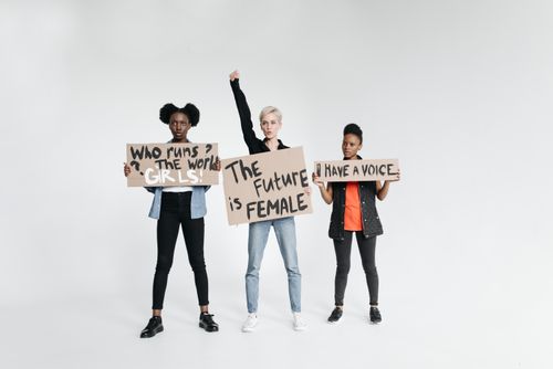 Free Three women holding signs advocating feminism and empowerment on a white backdrop, symbolizing unity and diversity. Stock Photo