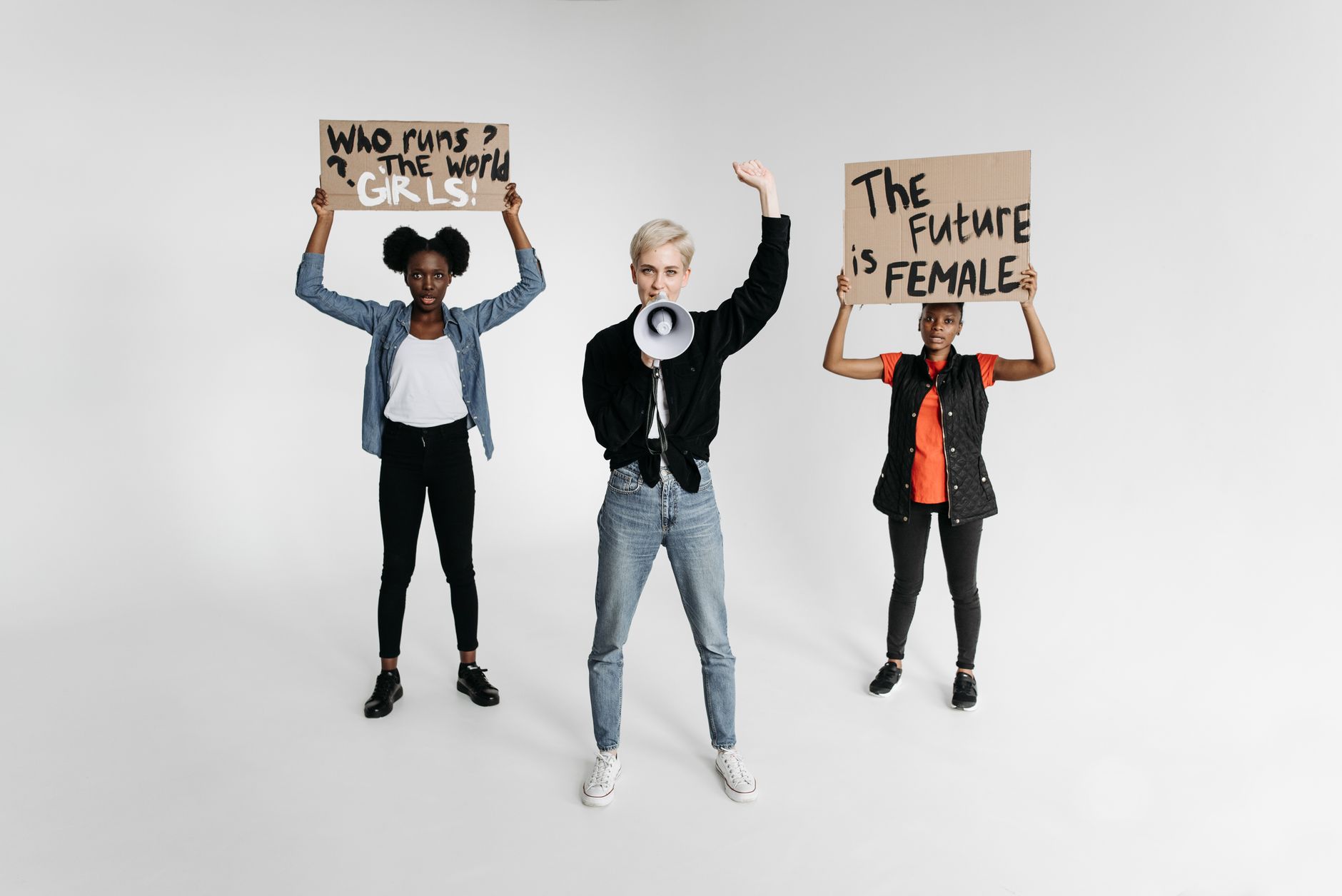 Three women holding feminist protest signs with powerful messages on a white background.