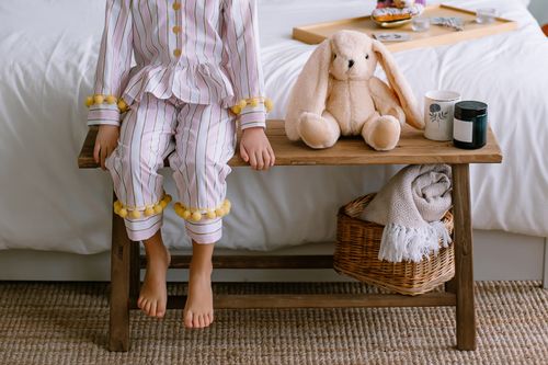 Free A child sitting on a bench in pajamas with plush toys in a cozy bedroom setting. Stock Photo