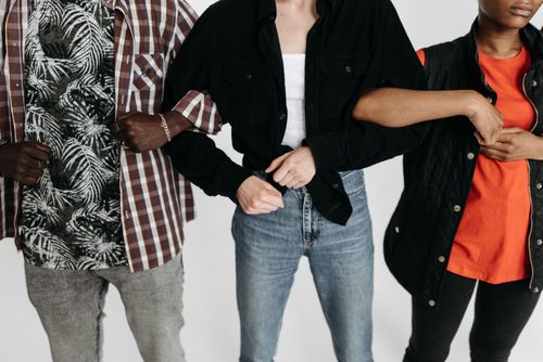 Free Close-up of three diverse individuals linking arms, showcasing unity and connection in a studio setting. Stock Photo