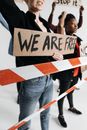 Person in Black Shirt Holding 'We are Free' Sign Behind Red and White Striped Ribbon