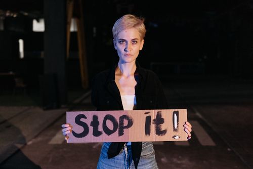 Free A woman holds a bold protest sign reading 'Stop it!' in a nighttime setting. Stock Photo