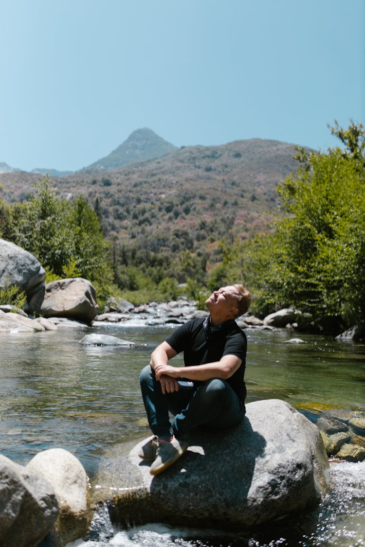 Man In Black Shirt Sitting On The Rock Near River