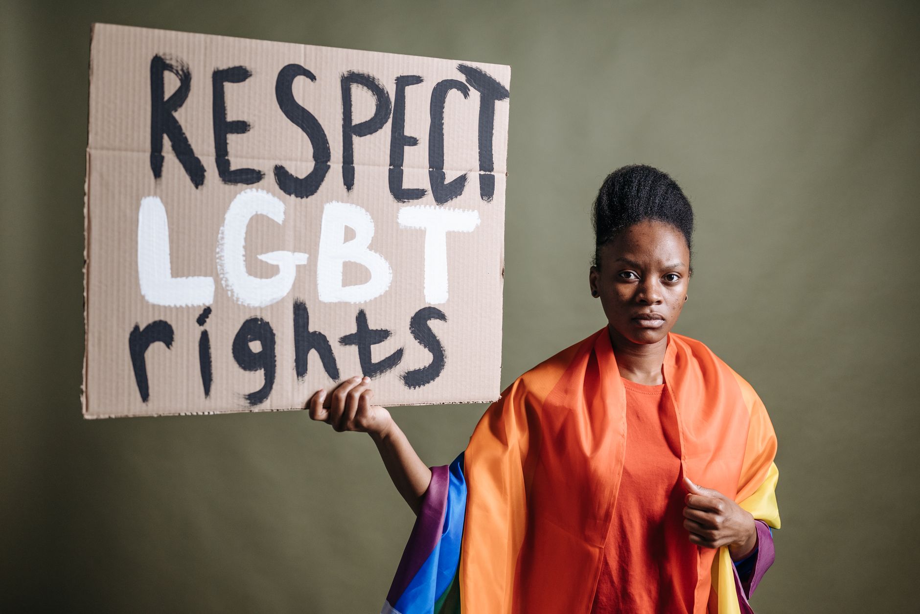 Gökkuşağı bayrağına sarılmış genç bir kadın, "Respect LGBT rights" yazılı karton bir pankart tutuyor
