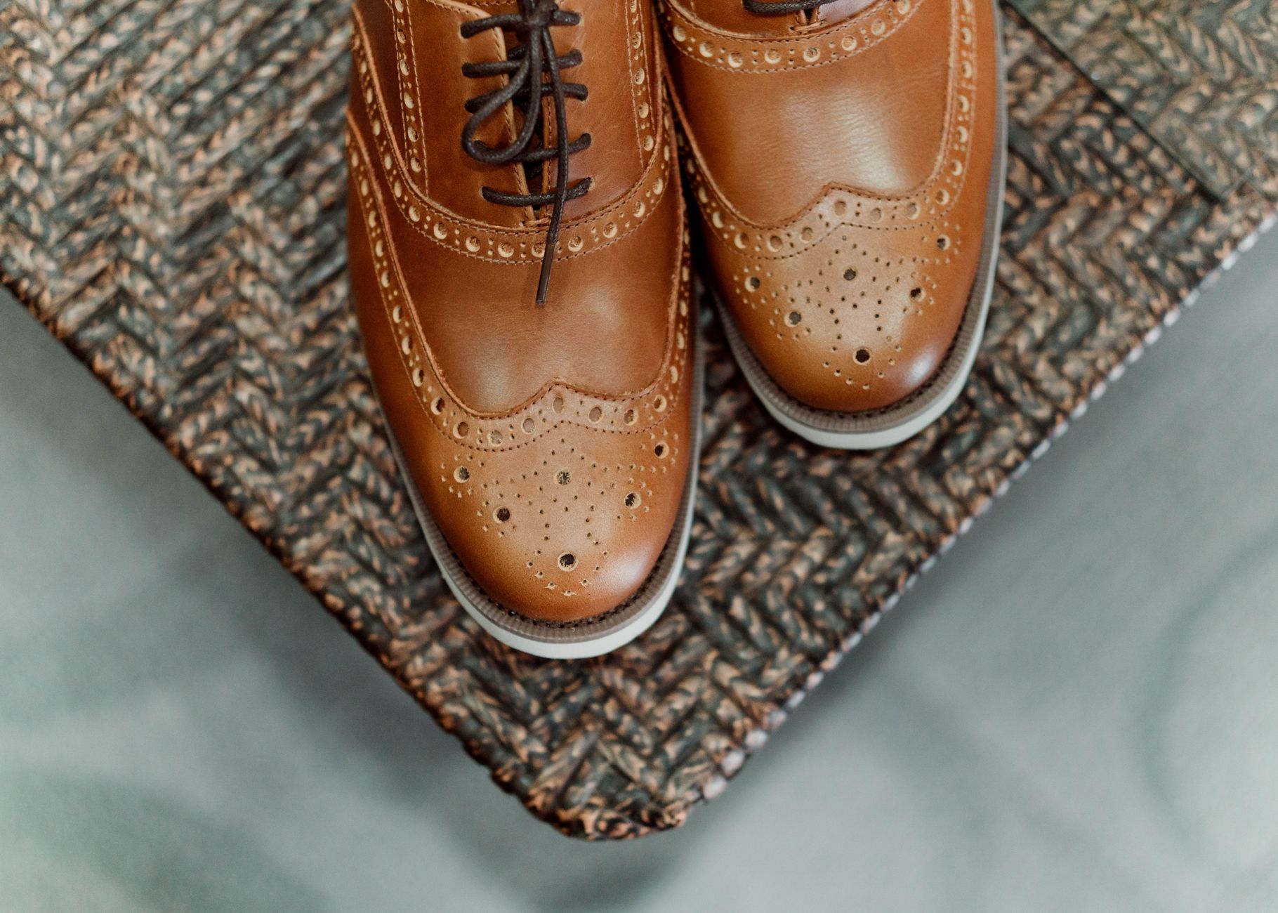 A close-up of stylish brown leather brogues with intricate design on a wicker surface.