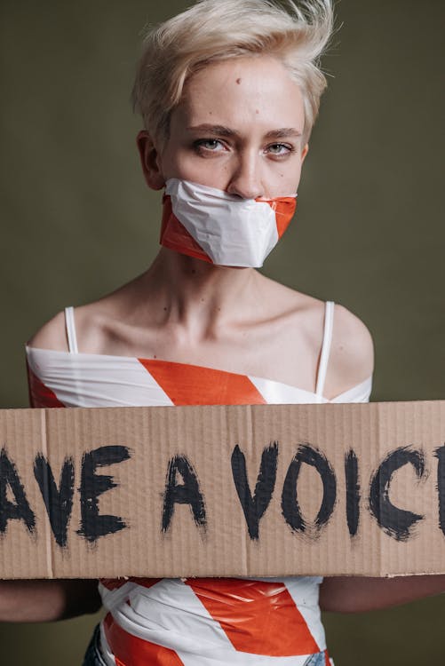 Free Woman with duct-taped mouth holding a protest sign advocating for voice and freedom. Stock Photo