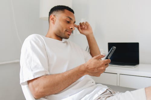 A Man in White Shirt Using a Smartphone while Sitting