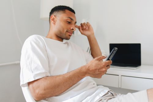 Free Casual man in white shirt browsing on smartphone indoors, showcasing modern lifestyle. Stock Photo