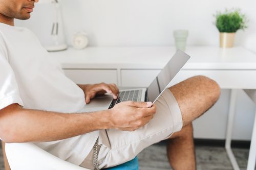 Free A man sitting relaxed at home using a laptop for work in a modern, bright interior. Stock Photo