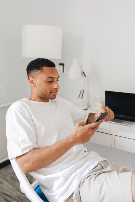 Casual young man in a white shirt using a smartphone at home office desk. Casual young man in a white shirt using a smartphone at home office desk.