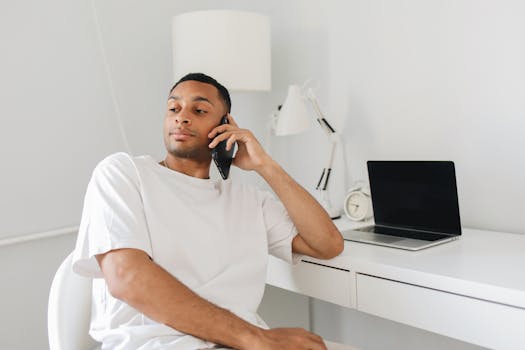 Confident man in white shirt on a phone call at a modern home office desk.
