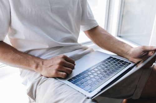 Free Close-up of a man using a laptop by a window, engaged in online study or work. Stock Photo