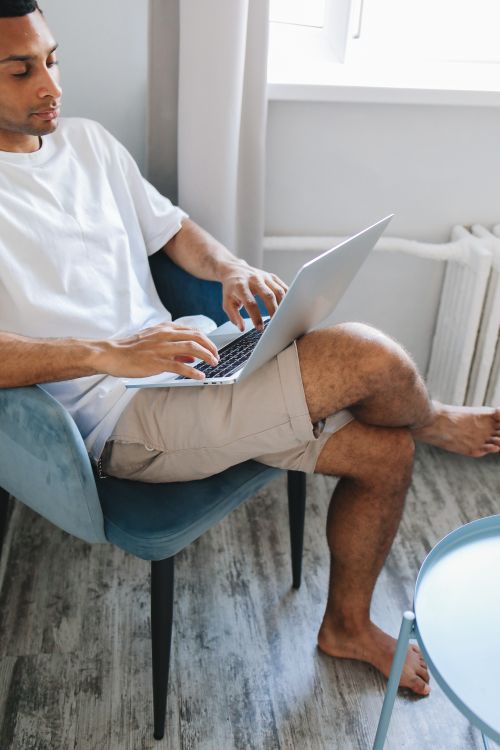 Free Casual adult man sitting indoors using a laptop with crossed legs in a calm home setting. Stock Photo