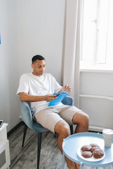 A man sits by the window reading a tablet, enjoying a relaxed home environment.