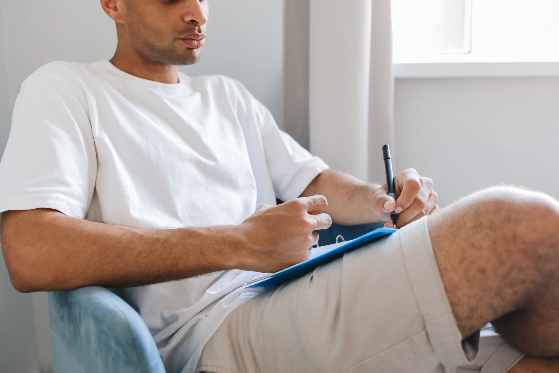 Casual indoor scene of a man in a white shirt writing notes with a pen.