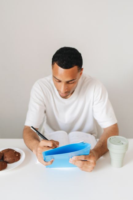 Adult man writing in a notebook while sitting at a table with snacks, focusing on indoor study time. Adult man writing in a notebook while sitting at a table with snacks, focusing on indoor study time.