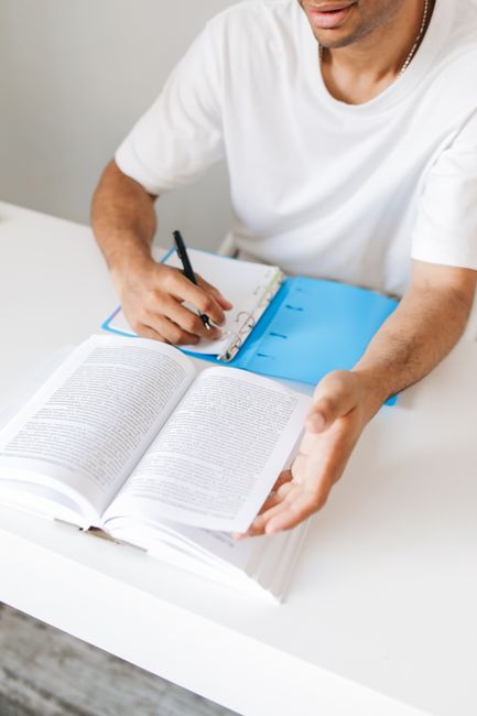An adult man takes notes from a book while studying at home, writing in a notebook. An adult man takes notes from a book while studying at home, writing in a notebook.