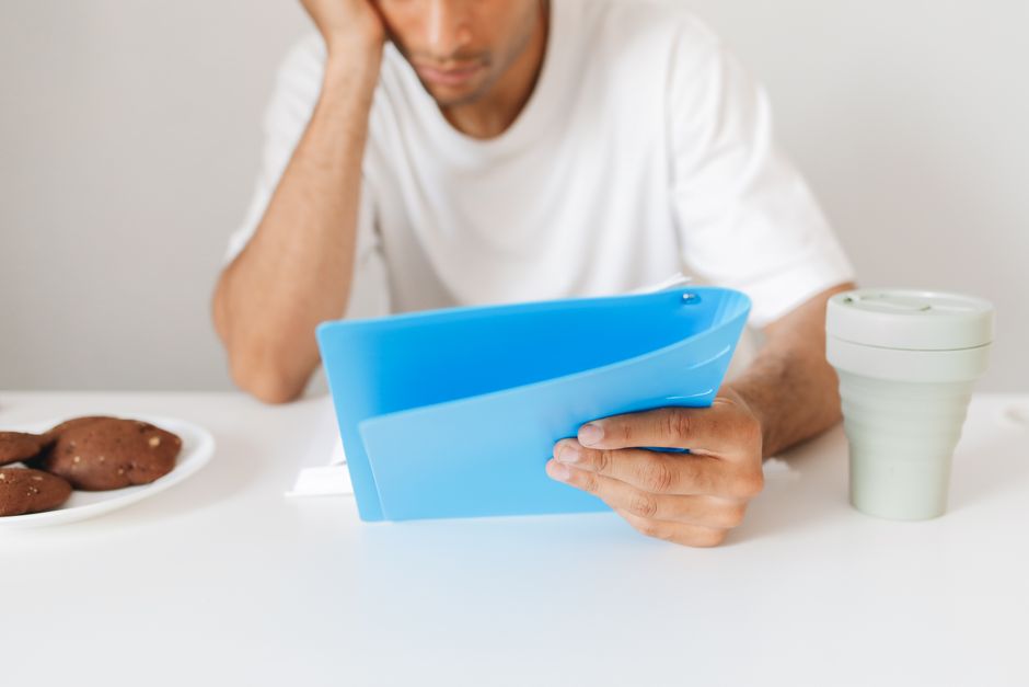 Man in white shirt focused on study materials with cookies and coffee on the table. Man in white shirt focused on study materials with cookies and coffee on the table.