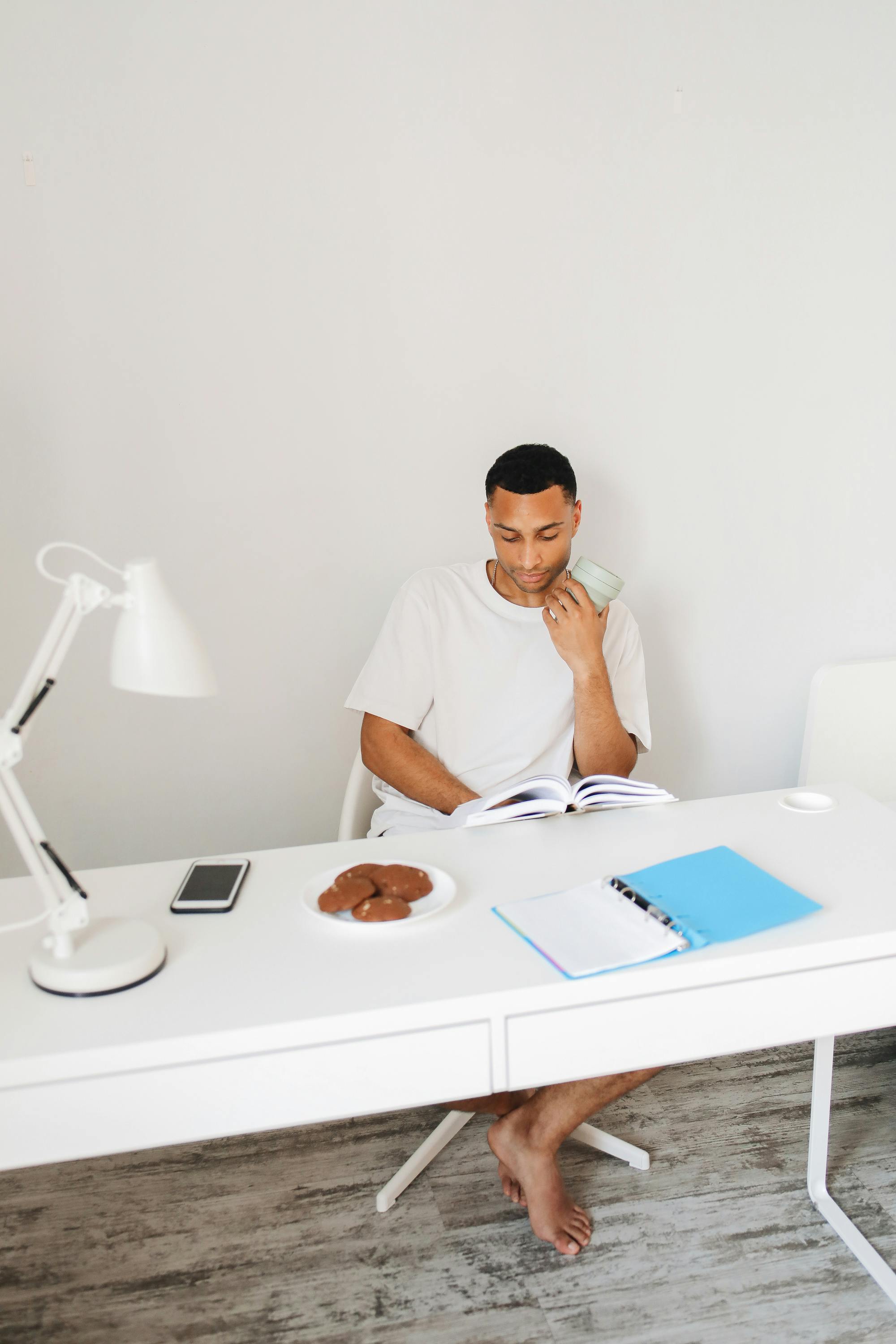 man reading a book while holding a glass cup