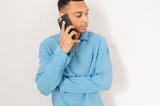 Man in blue long-sleeve shirt having a phone conversation, holding a smartphone.
