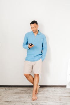 Casual man standing barefoot indoors using smartphone, relaxed lifestyle.