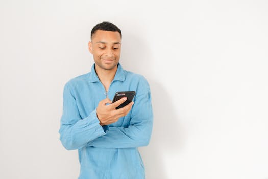 A smiling man in a blue shirt using a smartphone, isolated against a white background.