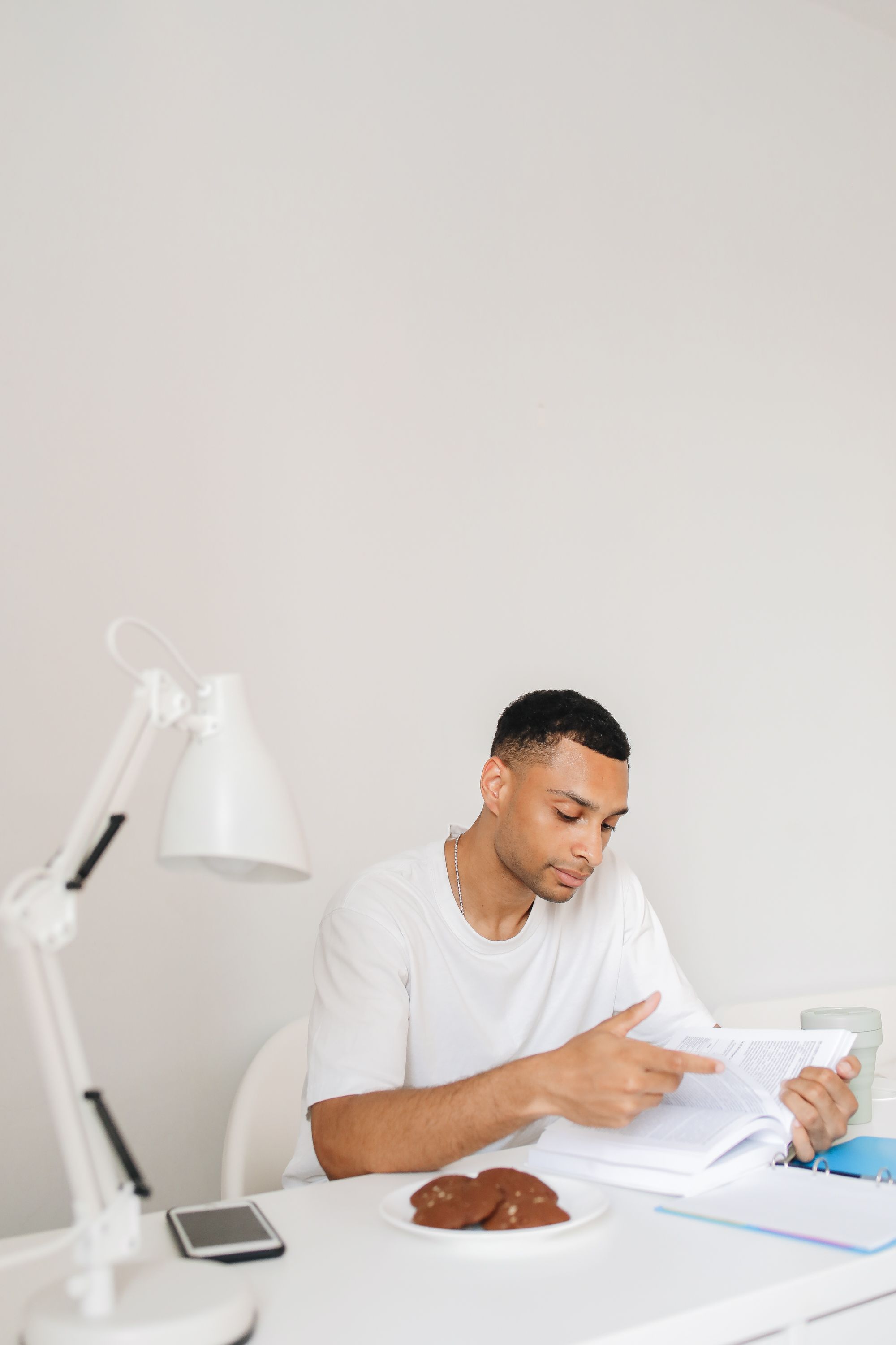 Adult man focuses on reading a book while seated indoors with a dessert on the table.