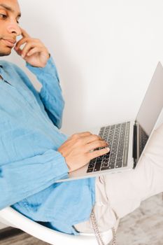 Casual man in blue shirt using a laptop while seated indoors, showcasing effortless productivity.