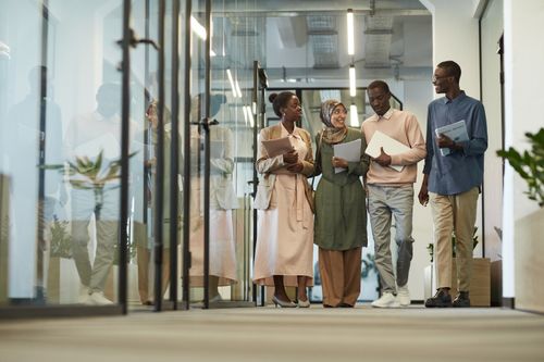 Free A diverse group of colleagues walking through a modern office hallway, engaged in conversation. Stock Photo