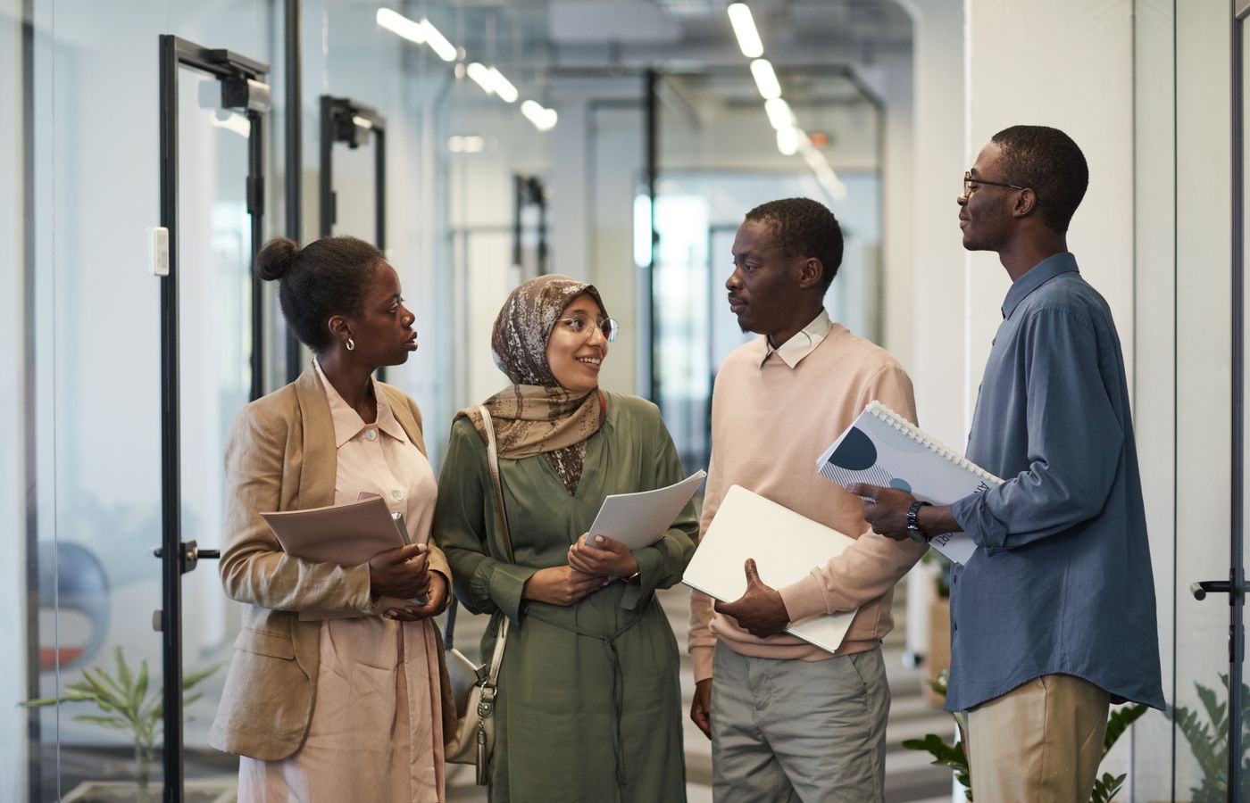 A diverse group of colleagues engaged in conversation in a modern office hallway.