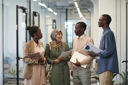 A diverse group of colleagues engaged in conversation in a modern office hallway.
