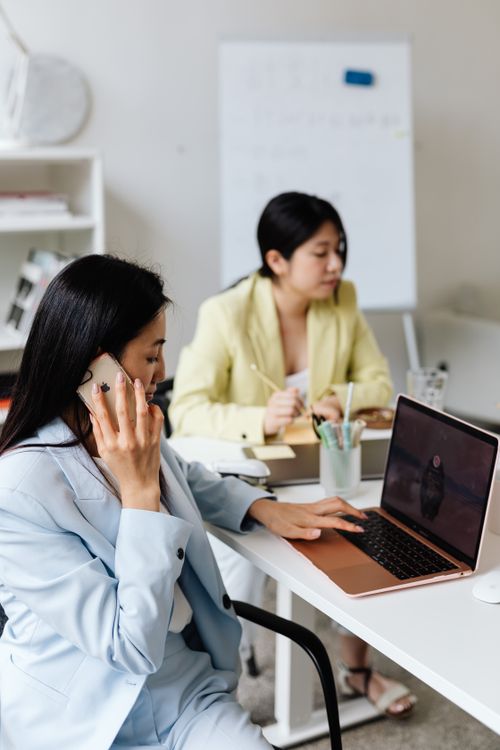 Free Two professional women collaborating in a modern office setting with laptops and smartphones. Stock Photo